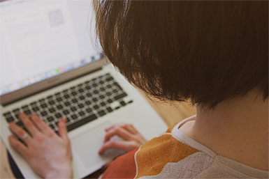 A view from over the shoulder of a woman sitting at her laptop, typing.