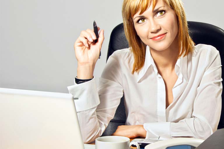 A woman sits at a desk with her computer, looking busy but confident.